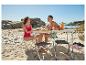 Couple pique-niquant sur la plage avec table et chaises pliantes, fruits et bouteille d'eau.