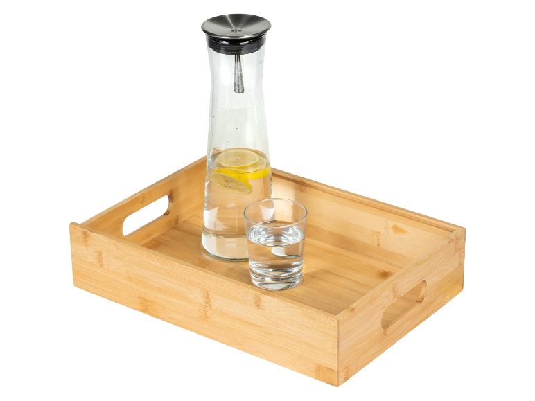 Carafe d'eau citronnée et verre sur un plateau en bambou.
