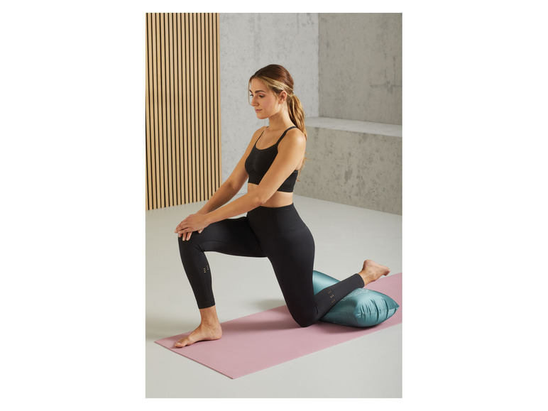 Een vrouw doet yoga op een roze mat met een blauwe kussen.