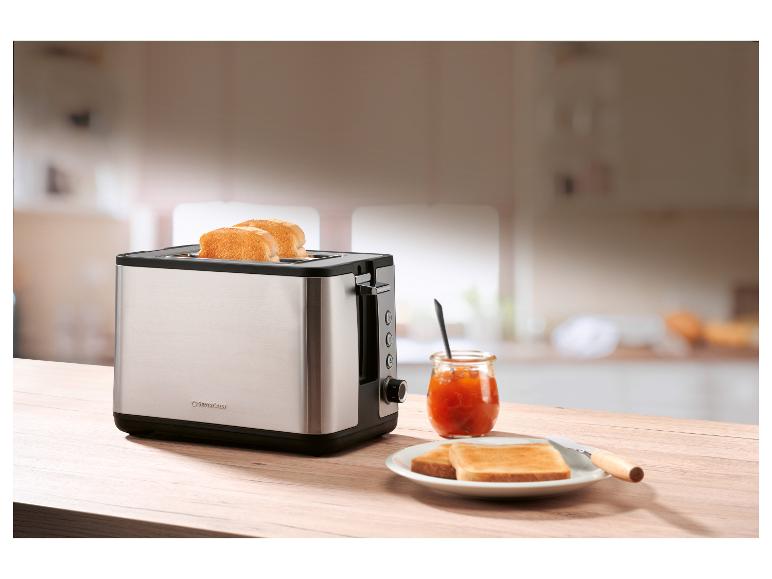 Een roestvrijstalen broodrooster met toast, jam en een mes op een houten tafel.