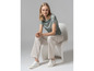 Een vrouw draagt een blauwe top met print, witte broek en witte sneakers.