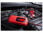 Un chargeur de batterie Ultimate Speed ​​rouge avec des pinces connectées à une batterie de voiture.