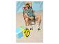 Homme en chemise à motifs, short, chaussettes et claquettes, tenant un ananas sur une plage de sable.