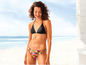 Een vrouw draagt een zwarte bikini met een tropische print aan de onderkant op het strand.