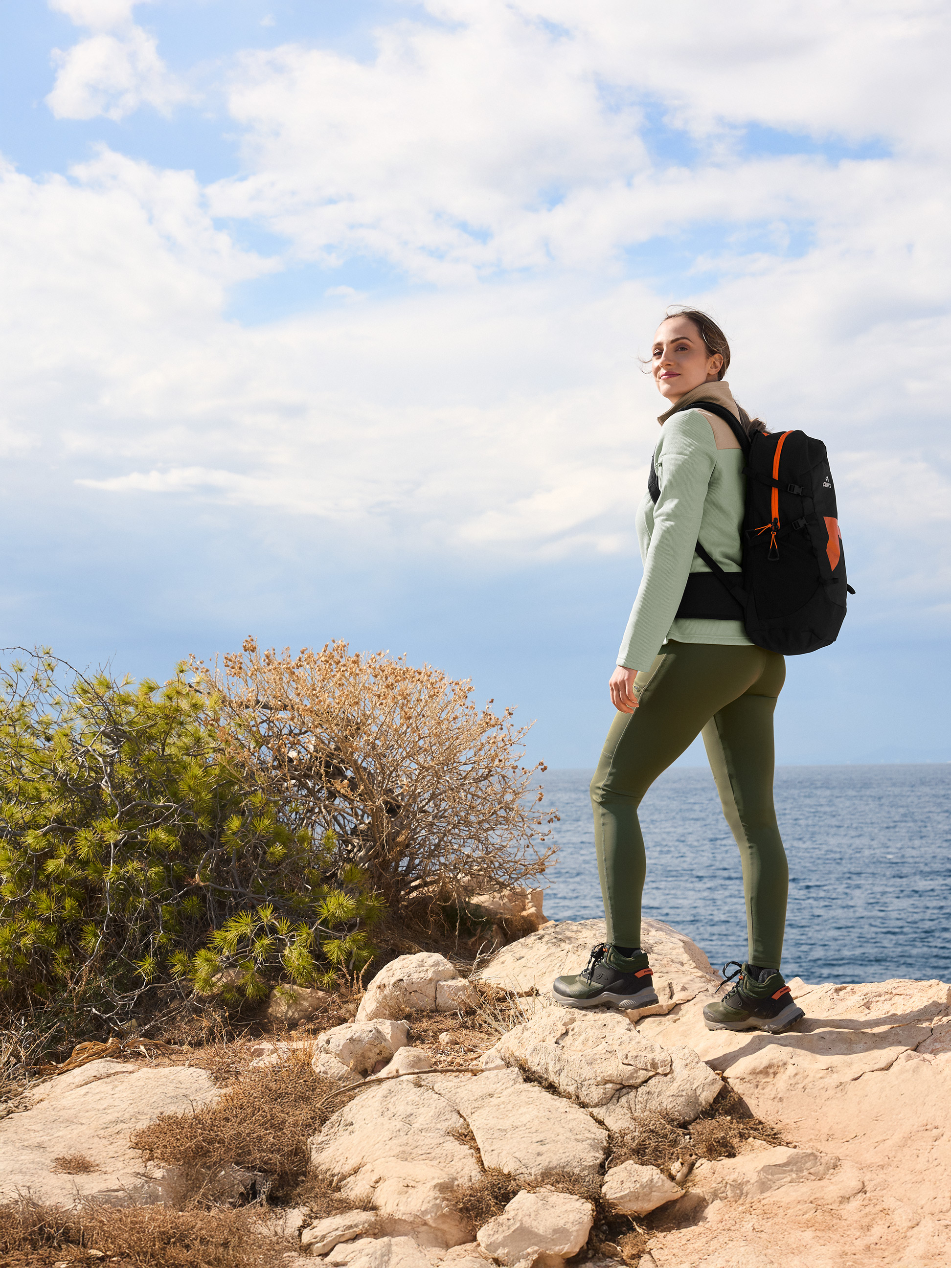 Vrouw in wandelkleding met rugzak op een rots bij de zee.