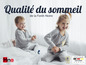 Deux enfants en pyjama gris sur un lit blanc, publicité pour les produits de sommeil Hne Schlafsysteme.