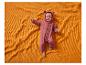 Lachende baby in een roze berenpak, liggend op een oranje deken.