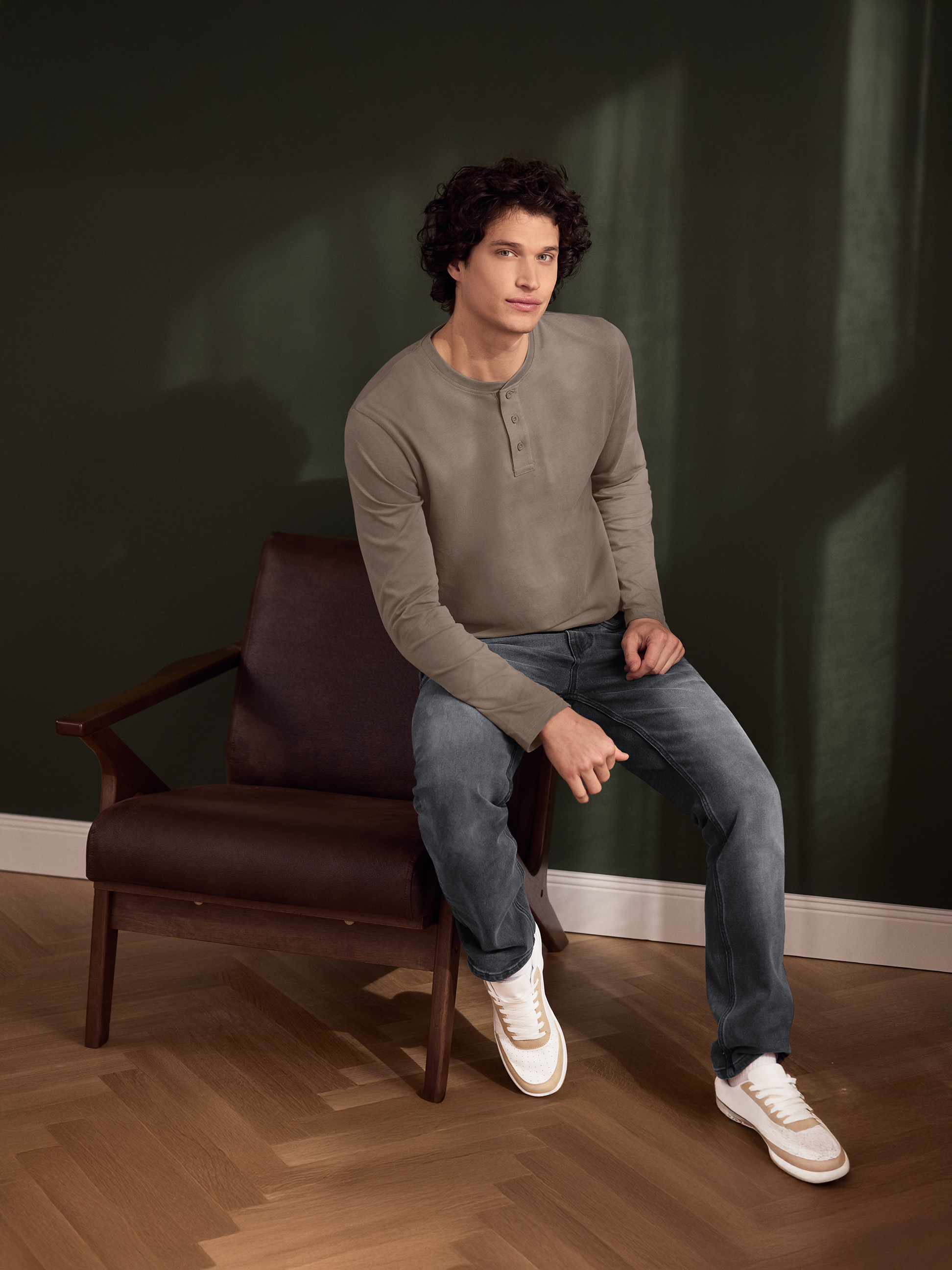 Man in bruin Henley-shirt en jeans zit op een leren stoel.