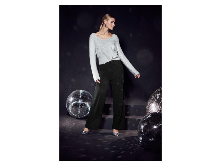 Femme en pull argenté et pantalon noir, avec des chaussures argentées, à côté de boules disco.