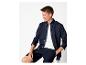Man in donkerblauw overhemd, wit T-shirt en donkerblauwe korte broek, zittend op een kruk.