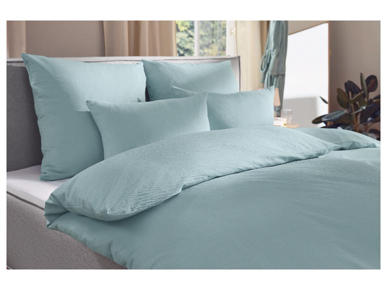 Mintgroen beddengoed met kussens op een bed in een slaapkamer met raam en plant.