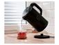 Bouilloire électrique noire versant de l'eau chaude dans une tasse de thé en verre.