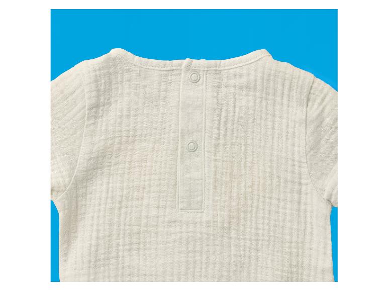 Witte baby romper met lange mouwen en knoopsluiting op de rug, tegen een blauwe achtergrond.
