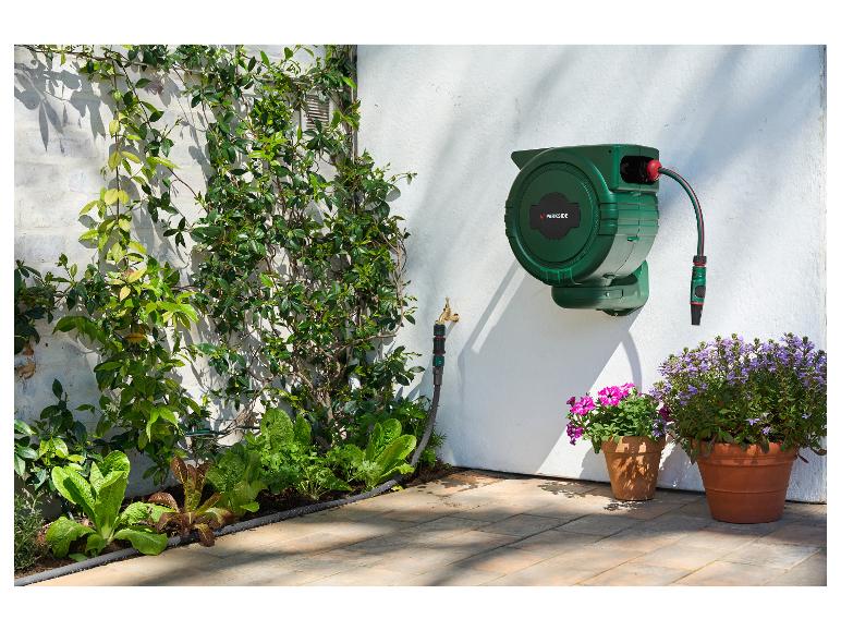 Dévidoir de tuyau PARKSIDE sur un mur blanc, avec des plantes et des fleurs en pot dans un jardin.