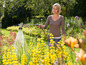 Une femme arrose des fleurs dans le jardin avec un tuyau d'arrosage.