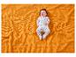 Un bébé en pyjama étoilé est allongé sur une couverture orange gaufrée.