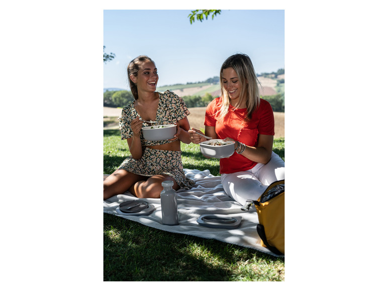 Deux femmes pique-niquent avec des boîtes à lunch et des bouteilles grises.