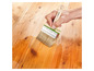 Een hand die een Parkside kwast met houten handvat gebruikt om hout te behandelen.