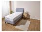 Un lit gris avec un protège-matelas blanc et une table de chevet en bois.