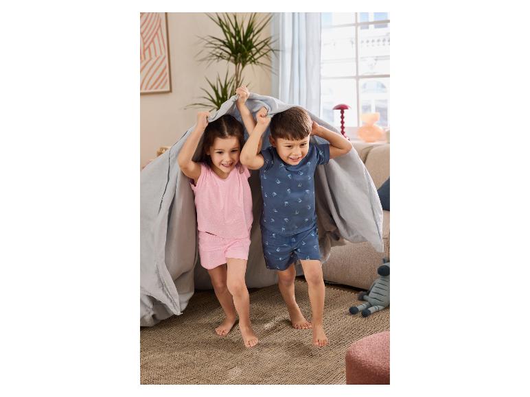 Deux enfants en pyjama d'été jouent sous un drap, souriants.