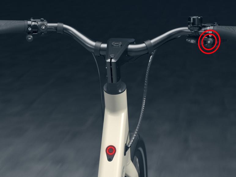 Het stuur van een witte elektrische fiets met een plusknop en een rode knop.
