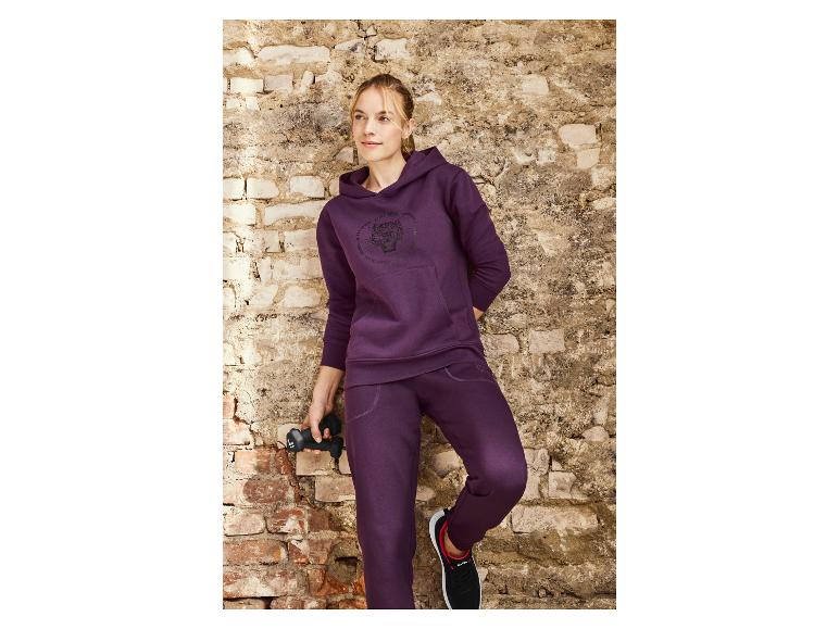 Een vrouw in een paarse hoodie en joggingbroek met een tijgerprint, houdt gewichten vast.