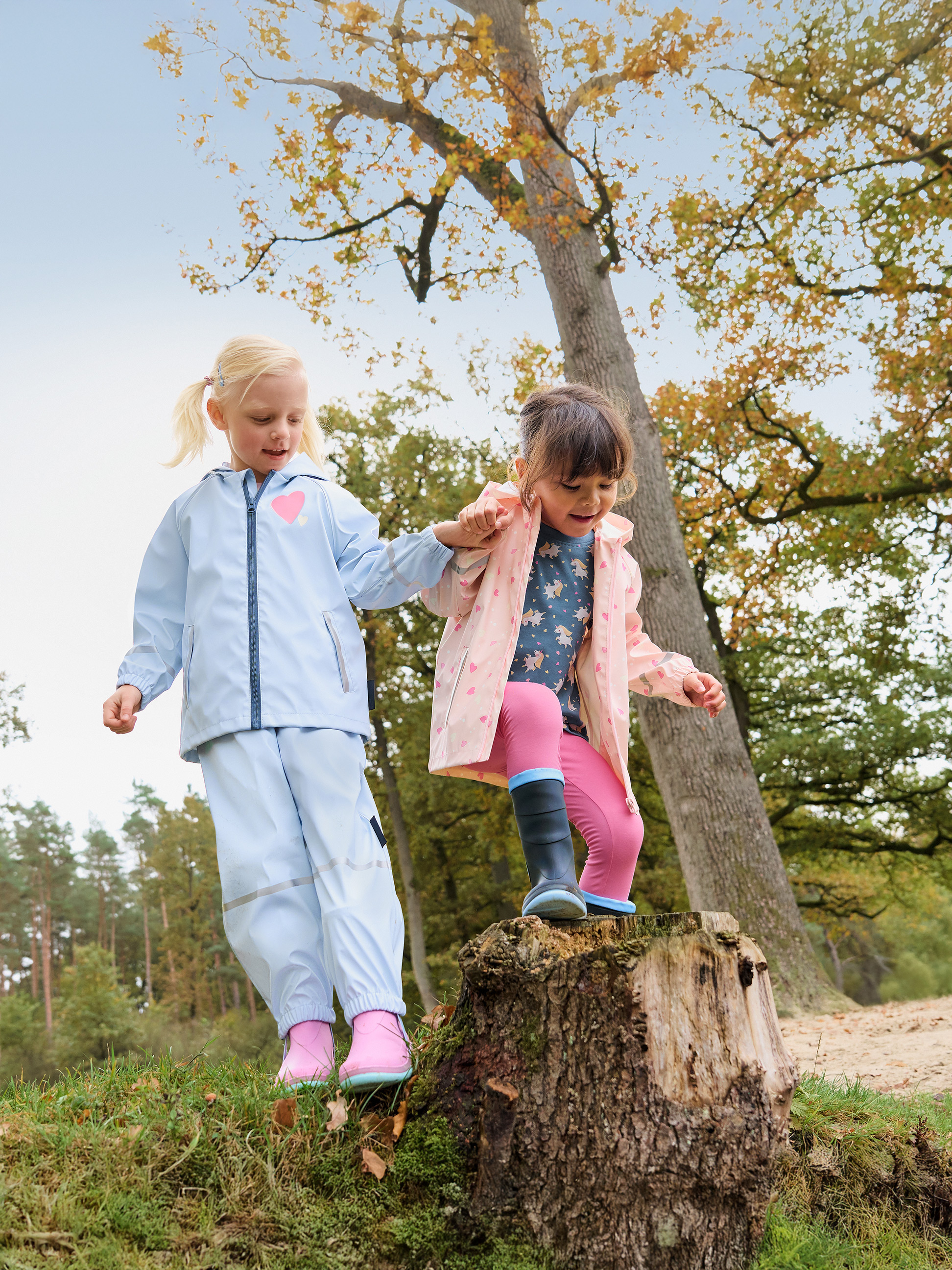 Deux enfants en cirés et bottes de pluie jouent sur une souche d'arbre dans la forêt.