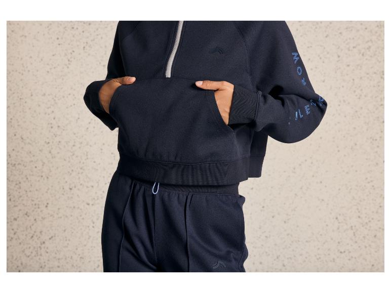 Een model draagt een blauwe hoodie en joggingbroek met een logo.