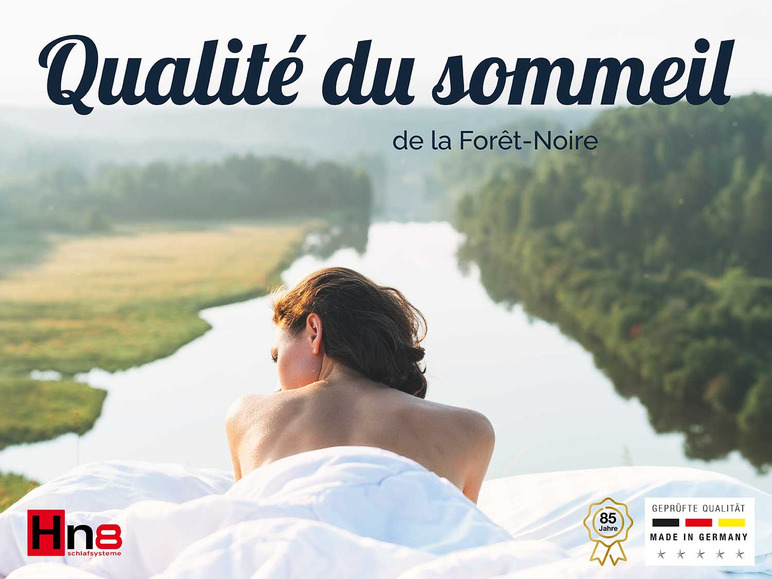 Femme dans un lit Hns avec vue sur une rivière et une forêt.