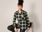 Een vrouw draagt een zwarte geruite blouse en zwarte broek.