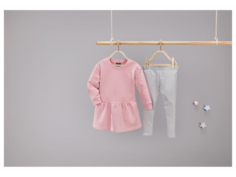Een roze jurk en grijze leggings hangen aan een houten hanger.