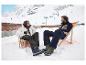 Twee mensen ontspannen in strandstoelen op sneeuw, gekleed in ski-jassen en -broeken.