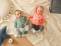 Deux bébés vêtus de vert et de rose sur une couverture blanche.