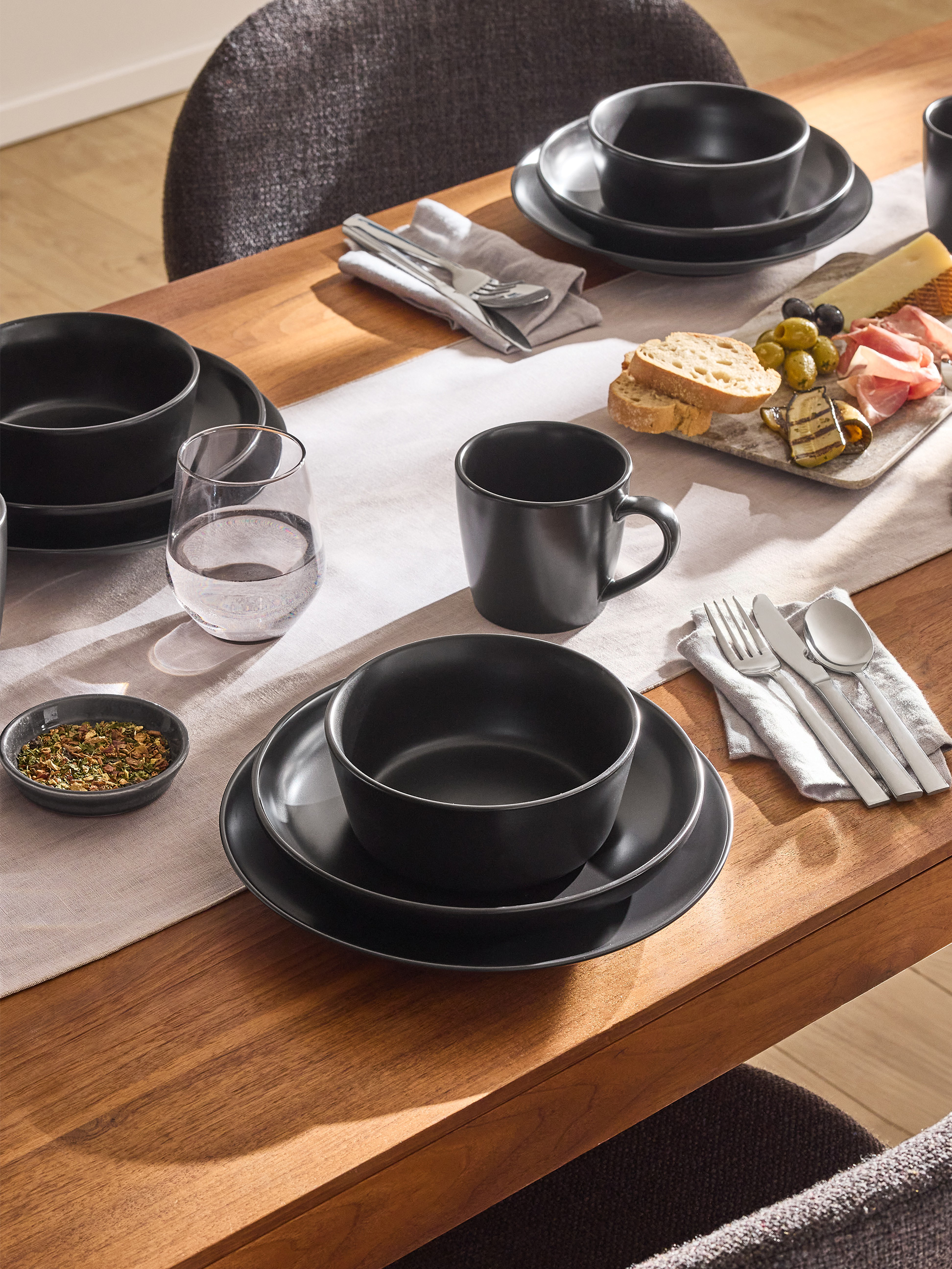 Table dressée avec vaisselle en grès noir, couverts et plateau d'antipasti.