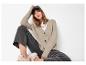 Vrouw draagt beige vest, donkere jeans, wit T-shirt, sneakers en pet.