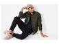 Homme en cardigan tricoté vert, pantalon noir et baskets beiges, assis sur le sol.