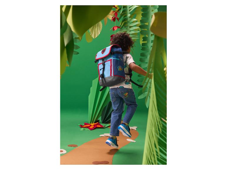 Kind met blauwe en rode rugzak, lopend op een pad in een papieren jungle.