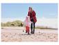 Une femme en manteau softshell outdoor rouge CRIVIT court sur la plage avec un enfant.