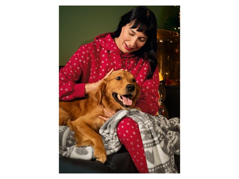 Une femme en pyjama rouge à motifs de flocons de neige câline un chien sur un canapé.