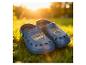 Paire de sabots bleus pour enfants avec personnages de dessins animés sur herbe verte au coucher du soleil.