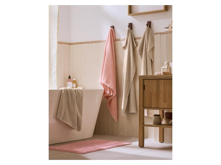 Salle de bain avec baignoire, serviettes roses et beiges, et meuble en bois.