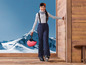 Een vrouw in ski-kleding met een helm in haar hand staat op een houten terras.
