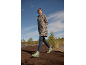 Vrouw in luipaardprint jas, blauwe jeans en groene laarzen loopt over een modderig pad.