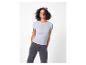 Vrouw met krullend haar, lichtblauwe top en donkere jeans.