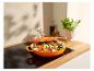 Een oranje Le Creuset gietijzeren pan met gebakken groenten op een inductiekookplaat.