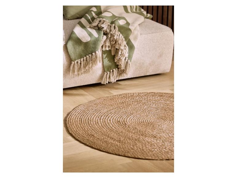 Beige bank met groene deken met bladeren en rond jute vloerkleed op houten vloer.