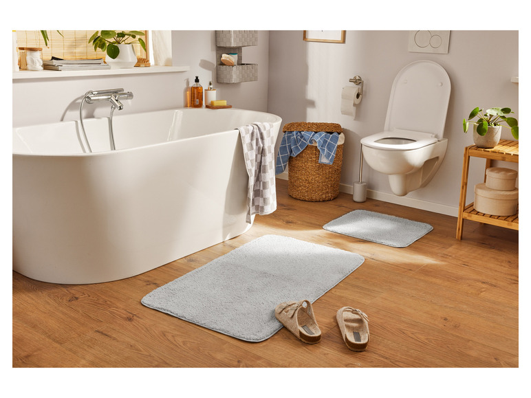Salle de bain avec baignoire, toilettes et deux tapis de bain.