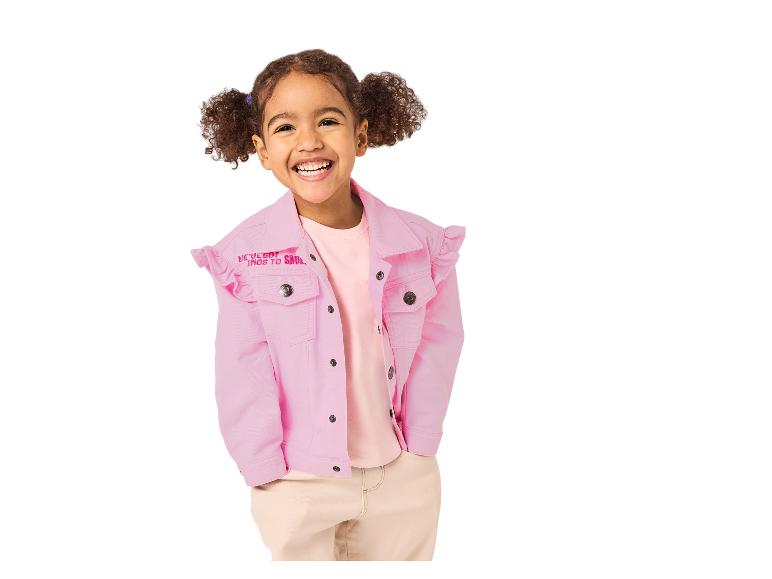 Lachend meisje in een roze spijkerjack met ruches en een beige broek.