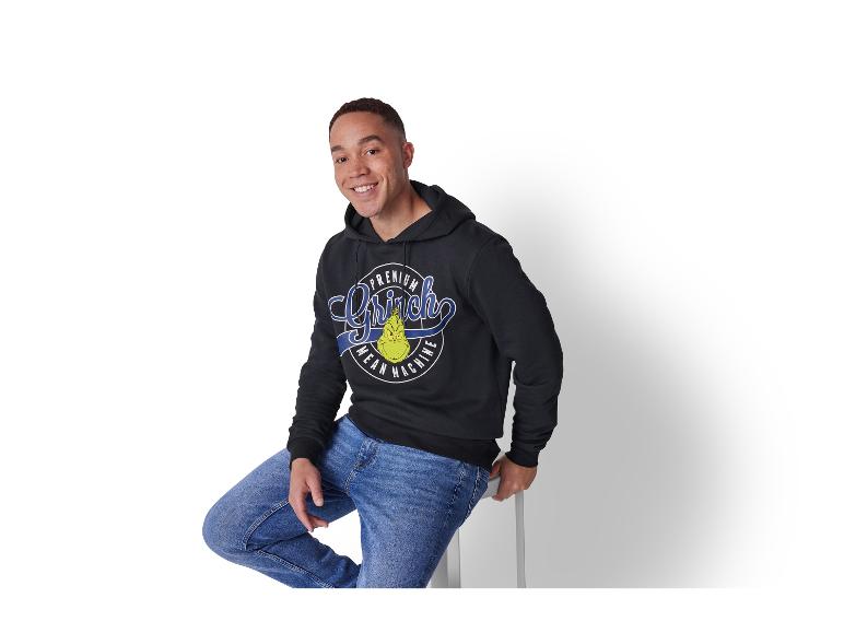 Lachende man in een zwarte Grinch hoodie en blauwe jeans.