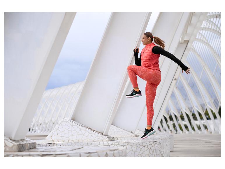 Femme en gilet et legging orange, sautant en extérieur.
